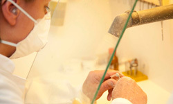 Zahntechnikerin arbeitet mit Schutzmaske an Zahnersatz in moderner Dentalwerkstatt.